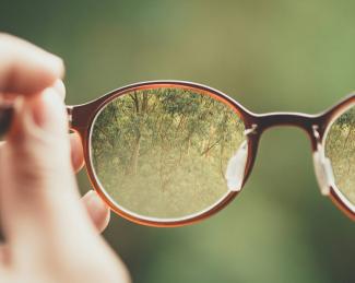 person holding brown eyeglasses with green trees background by Bud Helisson courtesy of Unsplash.